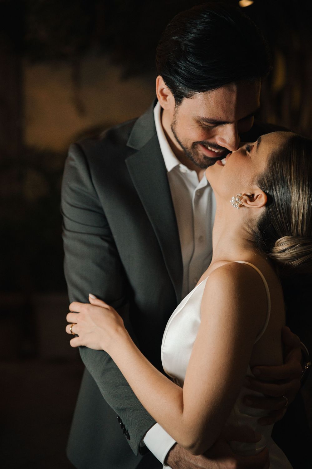 A romantic moment between newlyweds sharing an intimate kiss in formal wedding attire with moody lighting.