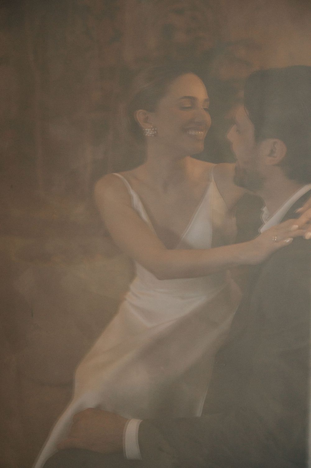 A couple embraces in a tender moment during their wedding celebration with soft atmospheric lighting.