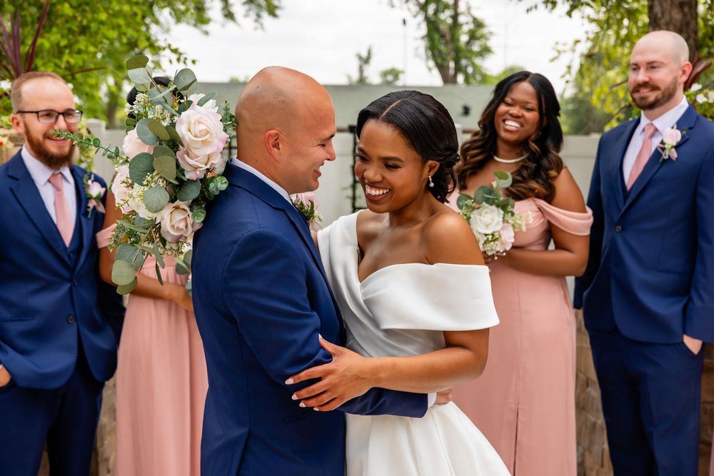Wedding party celebrates joyfully outdoors wearing coordinated navy and blush pink attire.