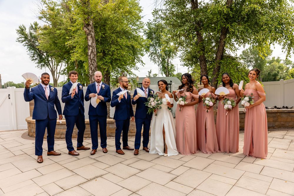 Wedding party lines up for formal photos on elegant stone terrace with trees in background at Villa Aletta in Omaha, NE.