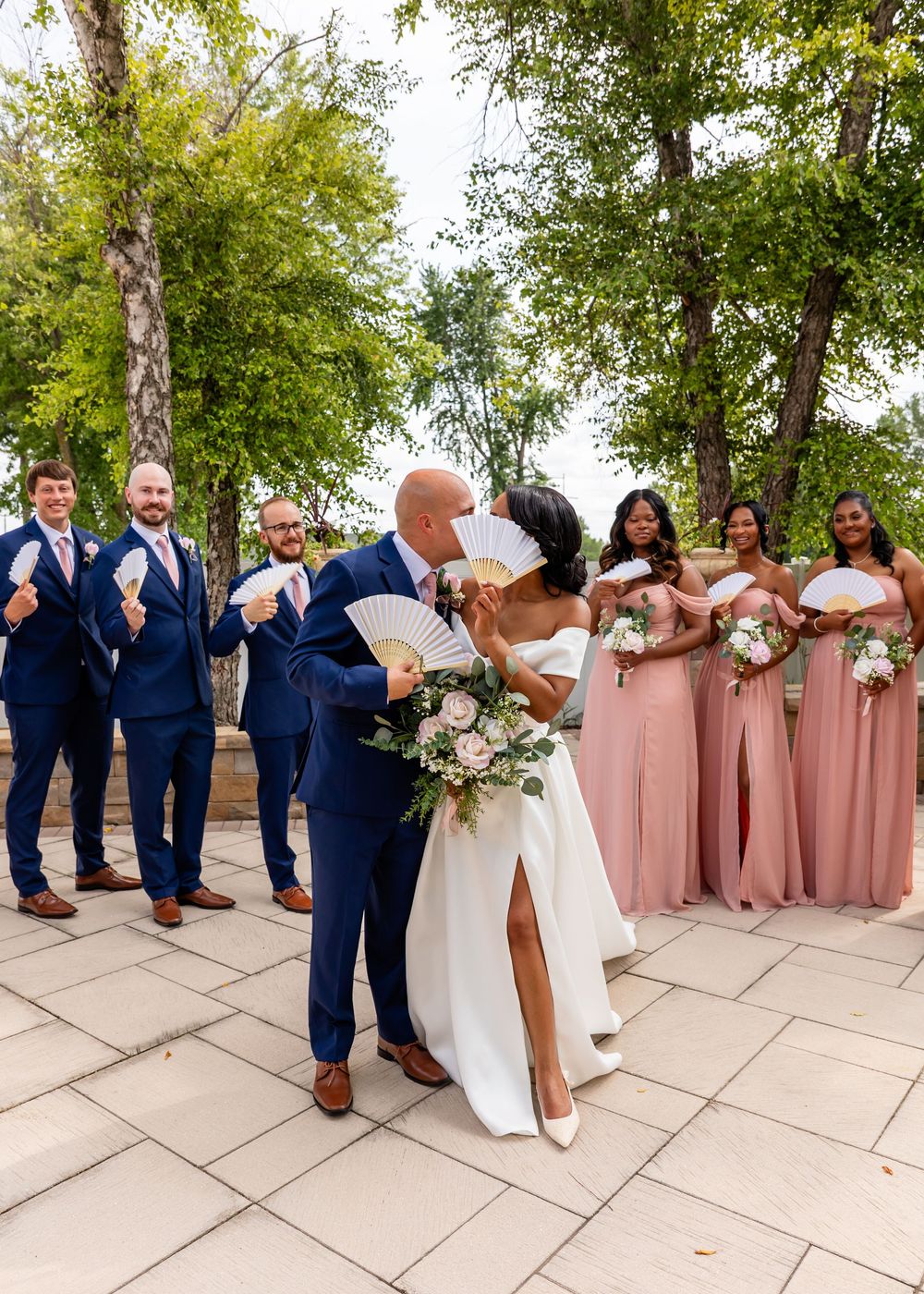 Bridal party in navy and blush pink attire poses playfully on stone terrace.