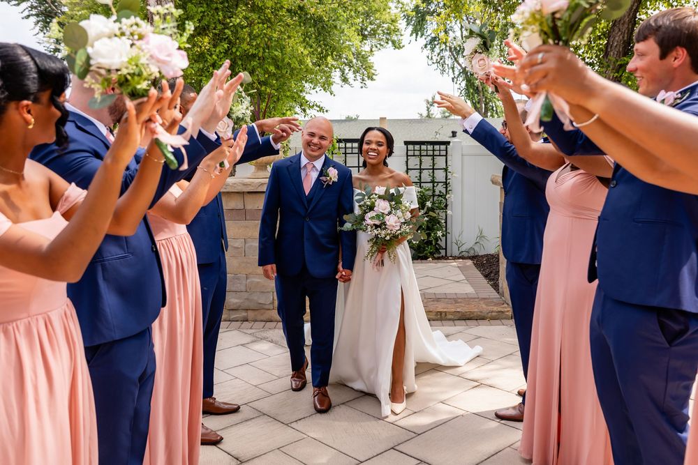 Joyful wedding party poses with decorative fans in coordinated navy and pink attire.