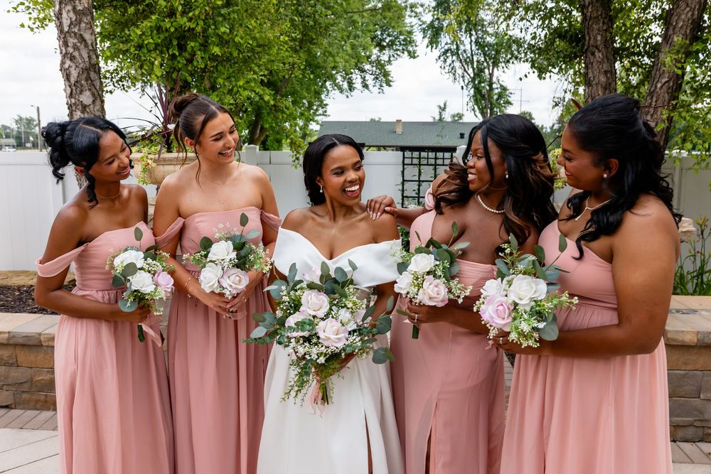 Bridesmaids in blush pink dresses hold white floral bouquets during outdoor photo session.