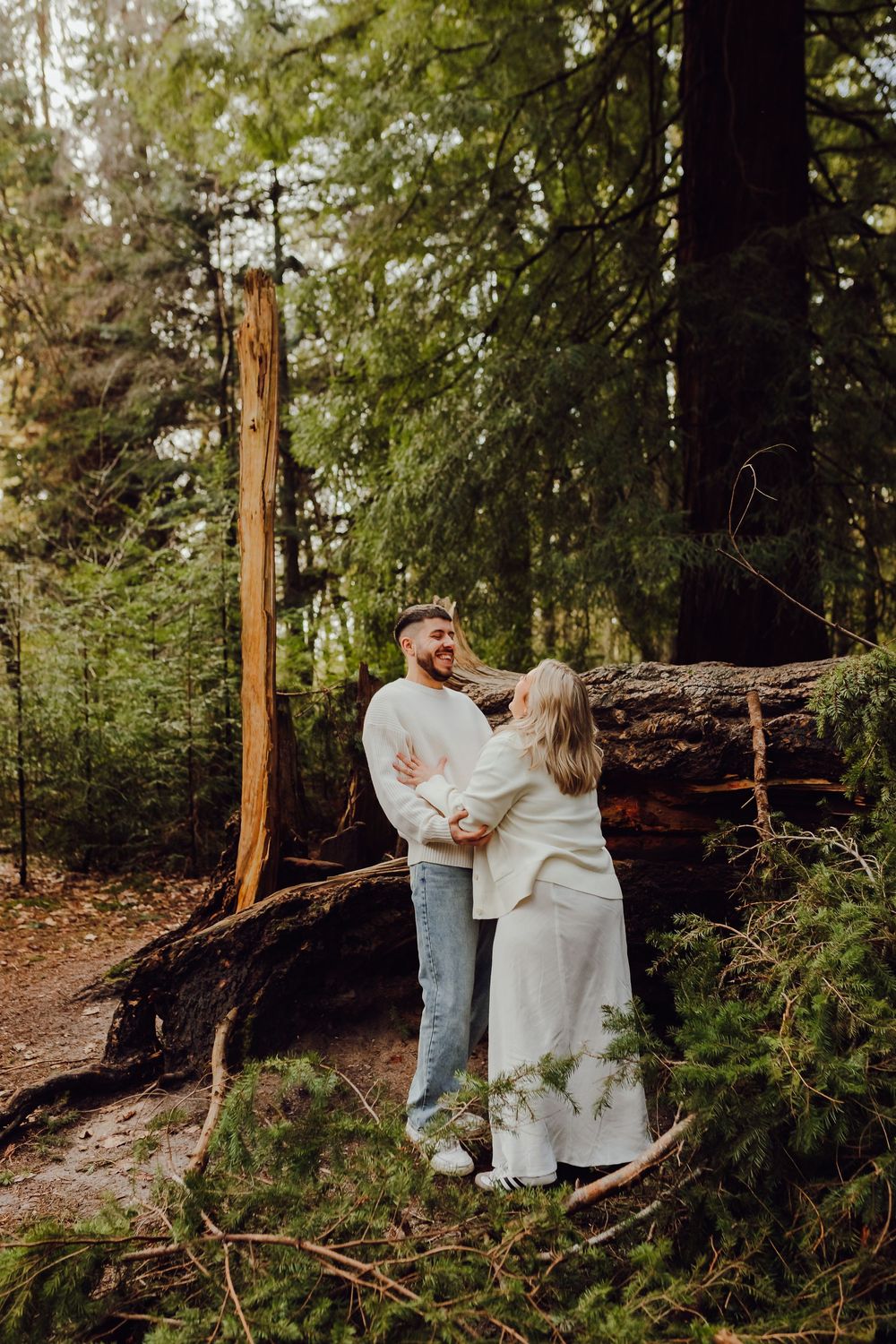 Hannah and Jordan are standing close together in a forest clearing.