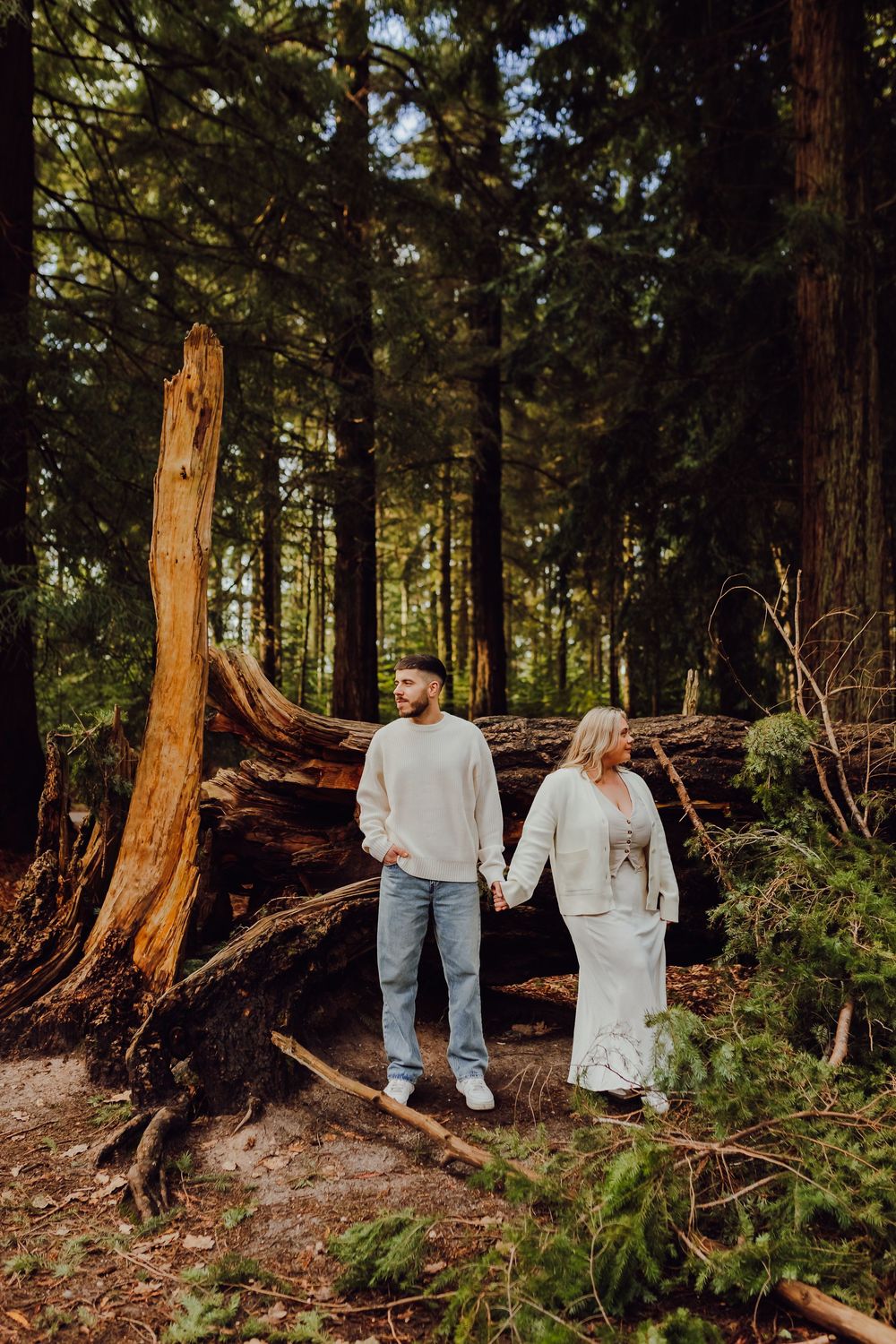 An engaged couple standing close together in a forest clearing.