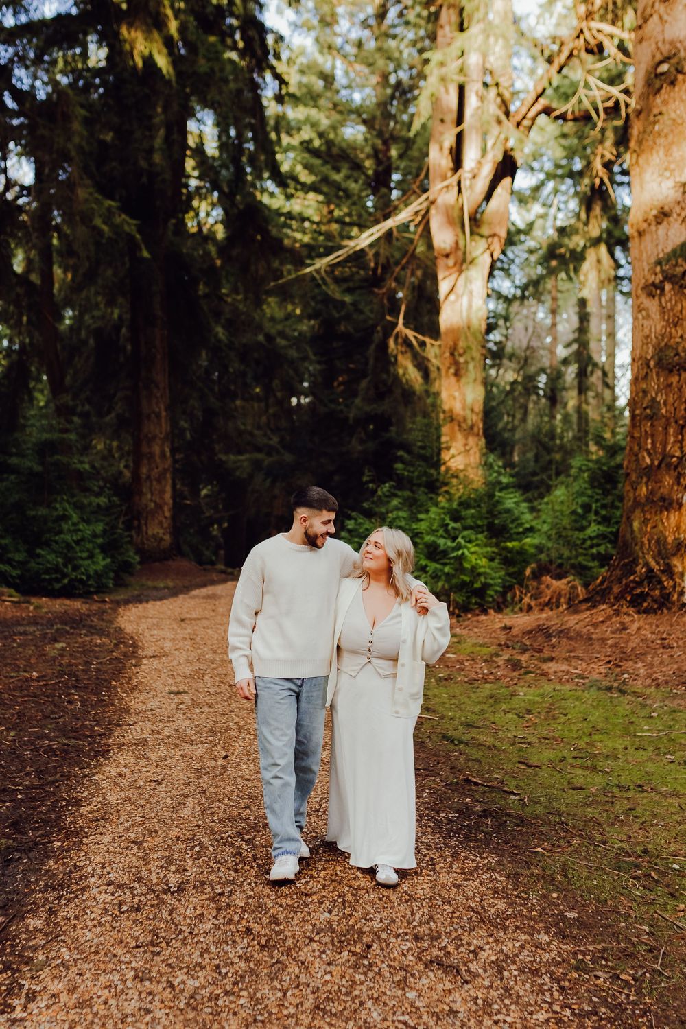 An engaged couple laughing together under trees on a winter afternoon.