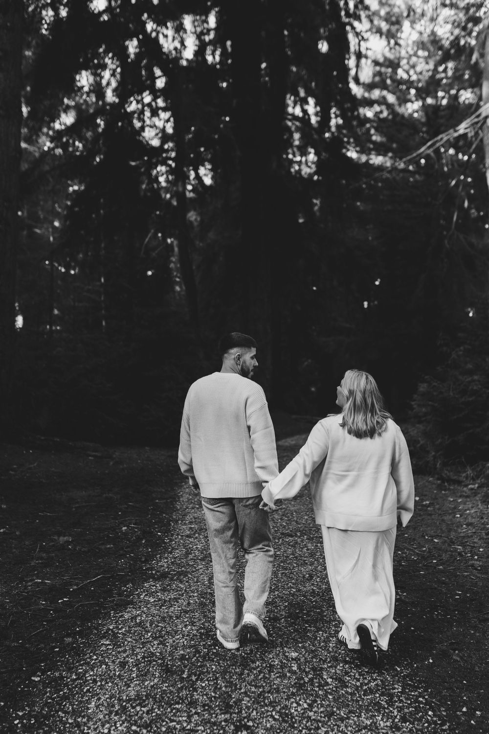 An engaged couple walking side by side on a woodland trail.