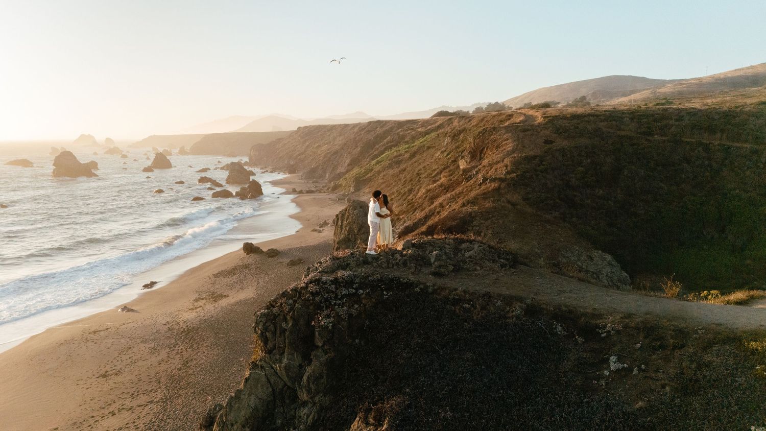 Panoramic coastal view of rocky cliffs and ocean waves at sunset.