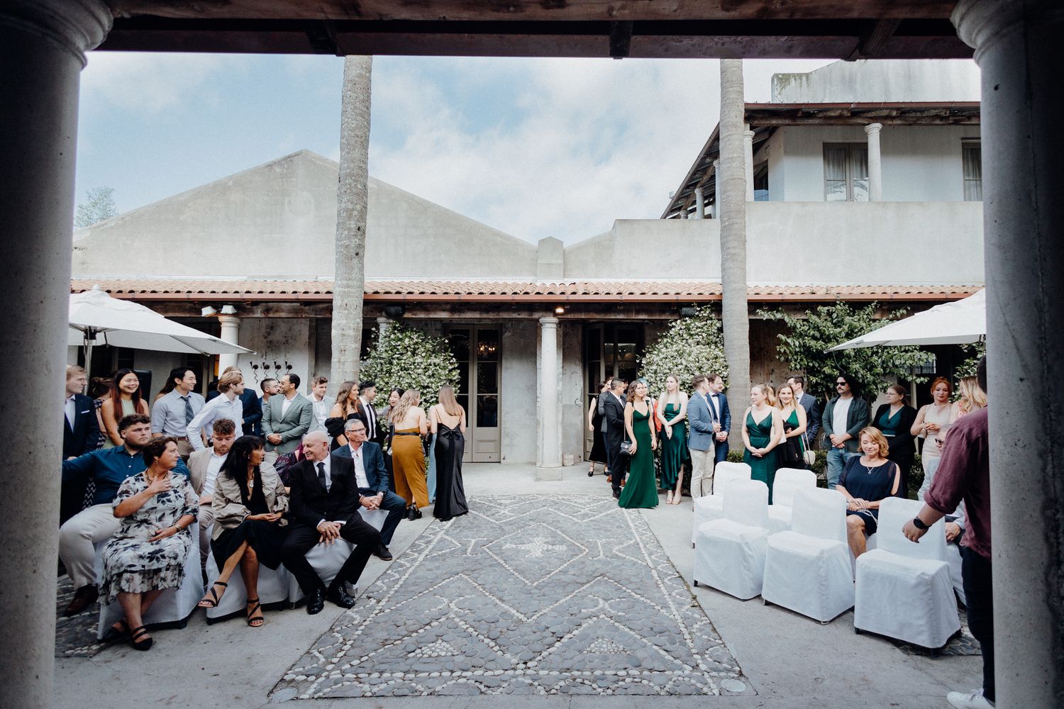 Wedding guests in a courtyard venue with terracotta roof architecture, captured by Apertured Media Auckland Wedding Photographer.