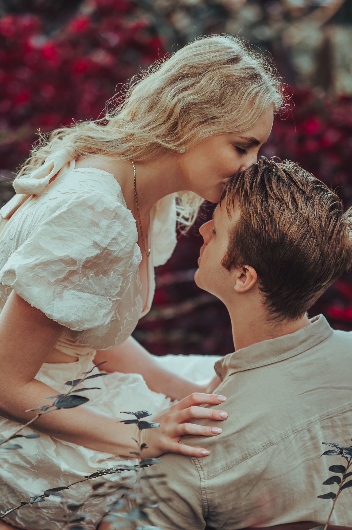 Intimate romantic moment shared between couple in front of burgundy flowers.