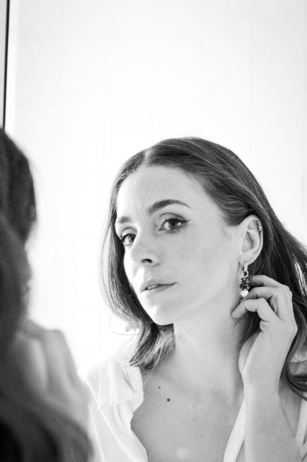 Ein schwarz-weiß Portrait der Braut beim Getting Ready, die sich und ihre Ohrringe im Spiegel betrachtet.
