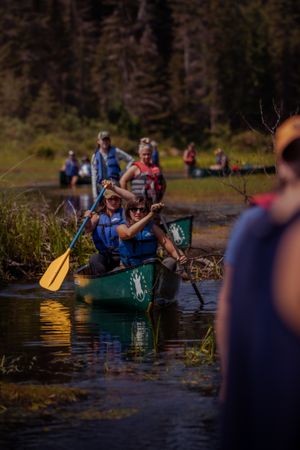 Kayakers paddle green canoes in scenic wilderness lake at sunset with forest background.