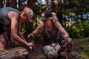 Two hikers kneel down to look at something interesting on a fallen log in the forest.