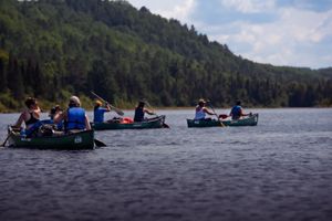 Paddlers in blue canoes navigate across a serene mountain lake surrounded by forested hills and calm waters.