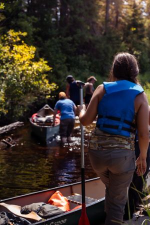Canoe paddlers in life vests prepare for an adventure on a tranquil forest lake during sunset.