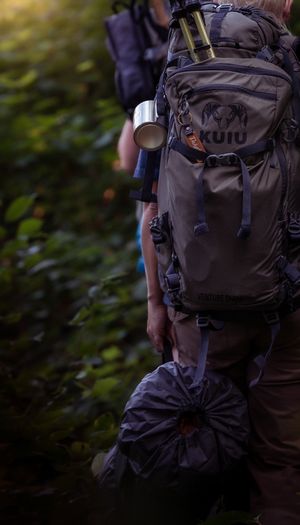 Close-up of a hiking backpack with gear attached against blurred natural background in low light conditions.