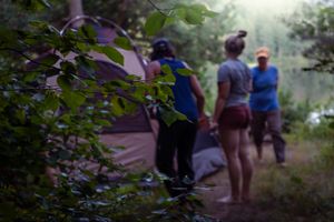 Campers set up a tent at a wooded campsite during a misty summer evening.