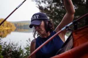 A person in a navy cap and tank top kayaking on a tranquil lake during sunset.