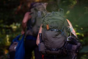 Closeup of a green and black hiking backpack with gear on a blurred outdoor trail background.