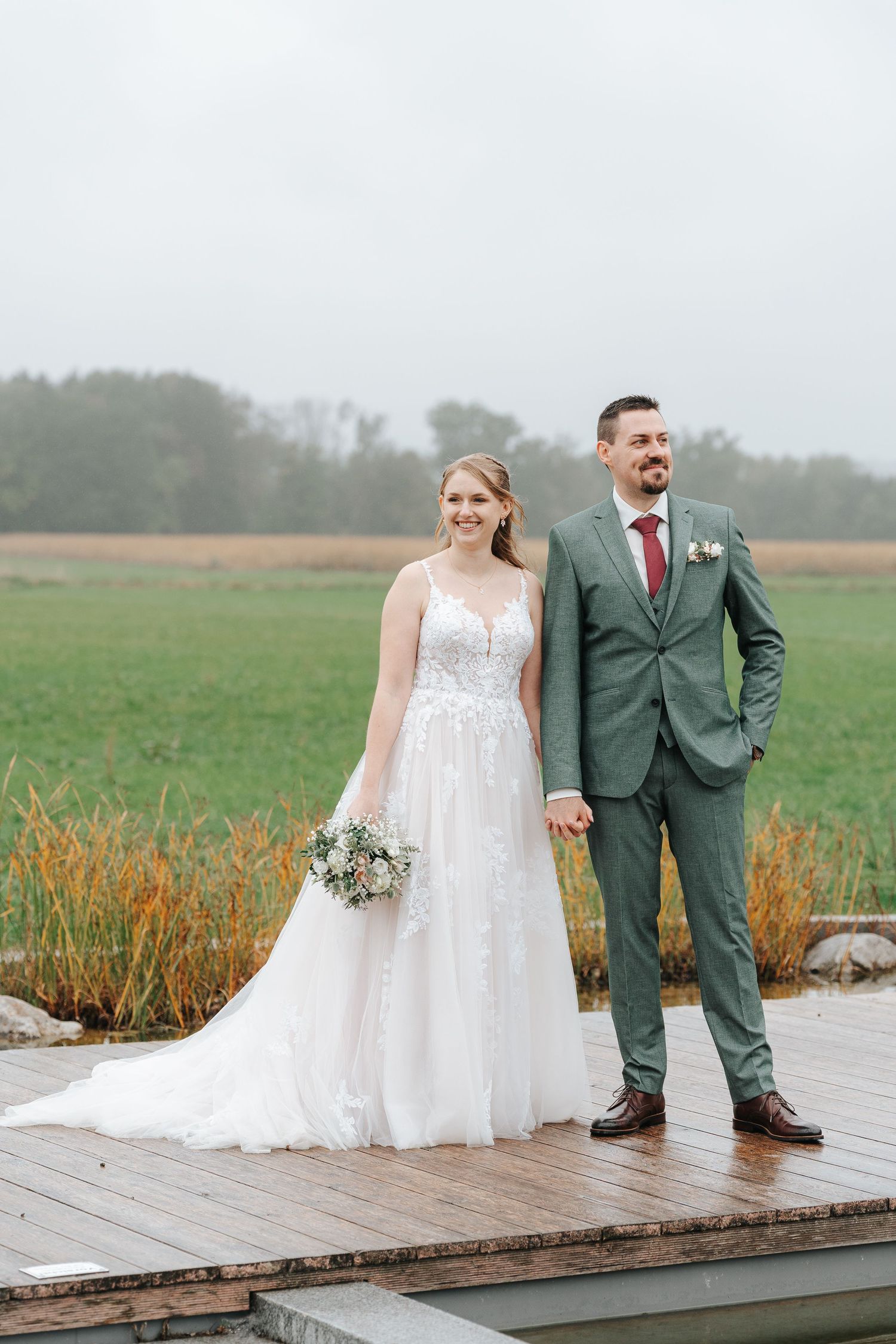 Wedding ceremony guests joyfully throw confetti at a couple on a wooden deck under a gazebo in an outdoor setting.