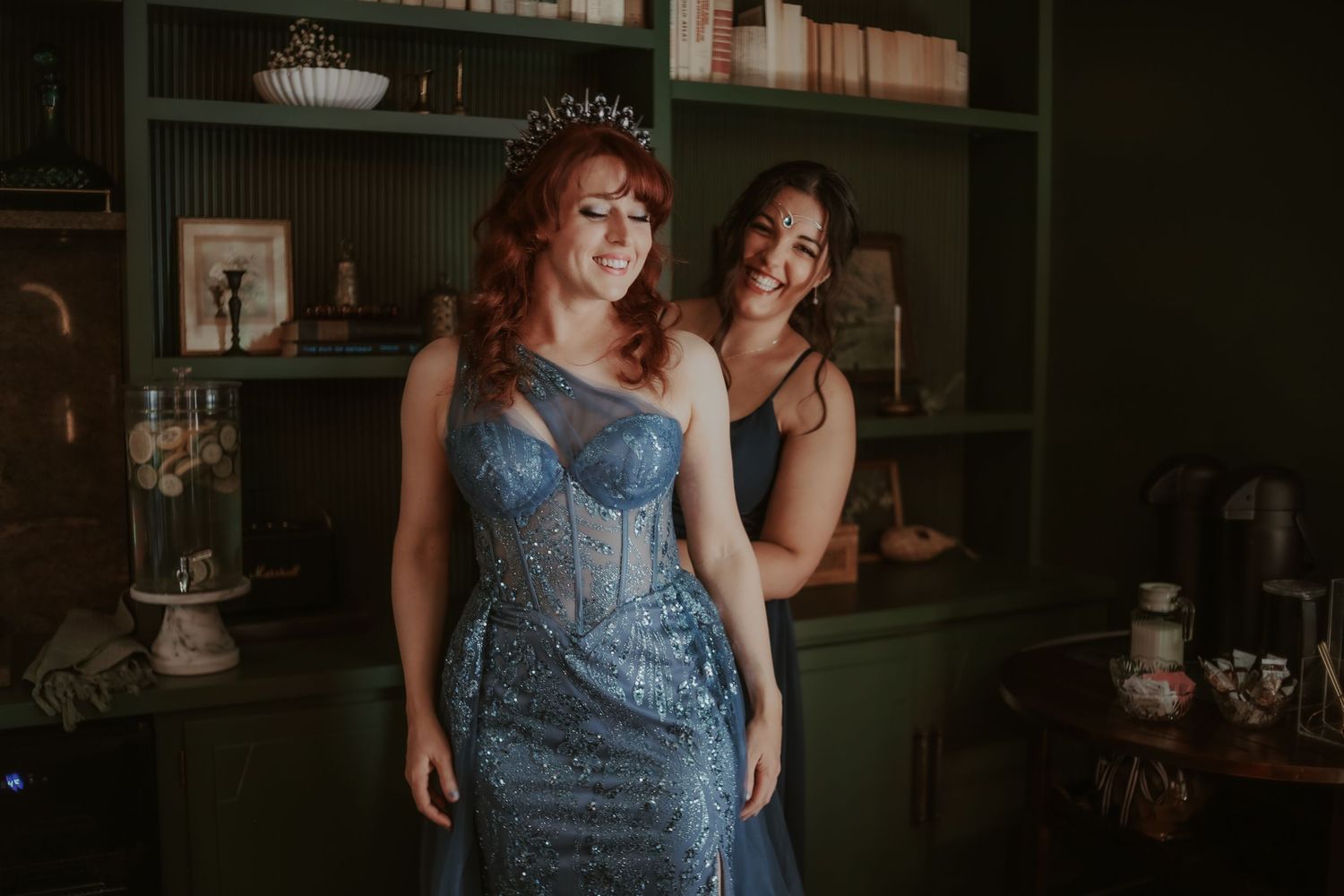Two people in elegant attire pose together in a dimly lit room with vintage decor.