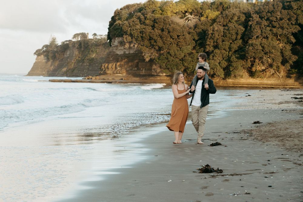 A couple walks along a scenic beach with dramatic cliffs in the background.