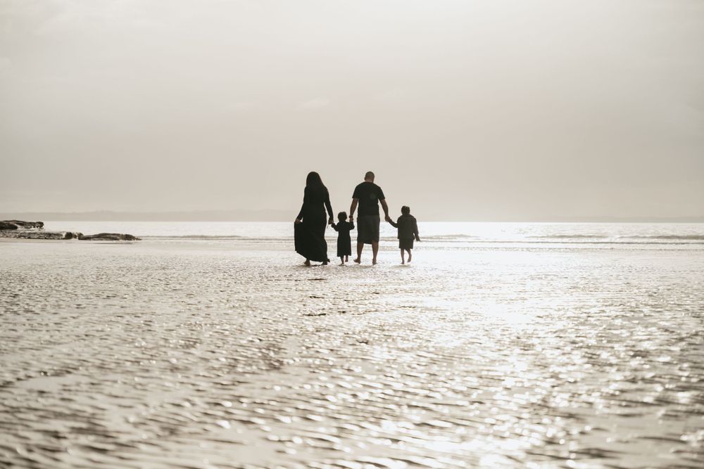 Silhouettes of a family walking together on a beach during sunset.