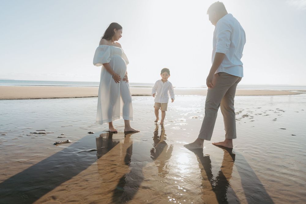 Family stands together at water's edge during sunset creating long shadows on wet sand.