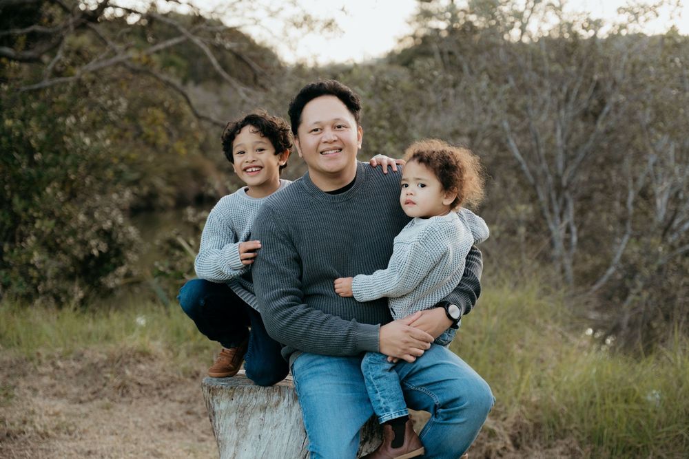 A playful outdoor family portrait in a natural hillside setting.