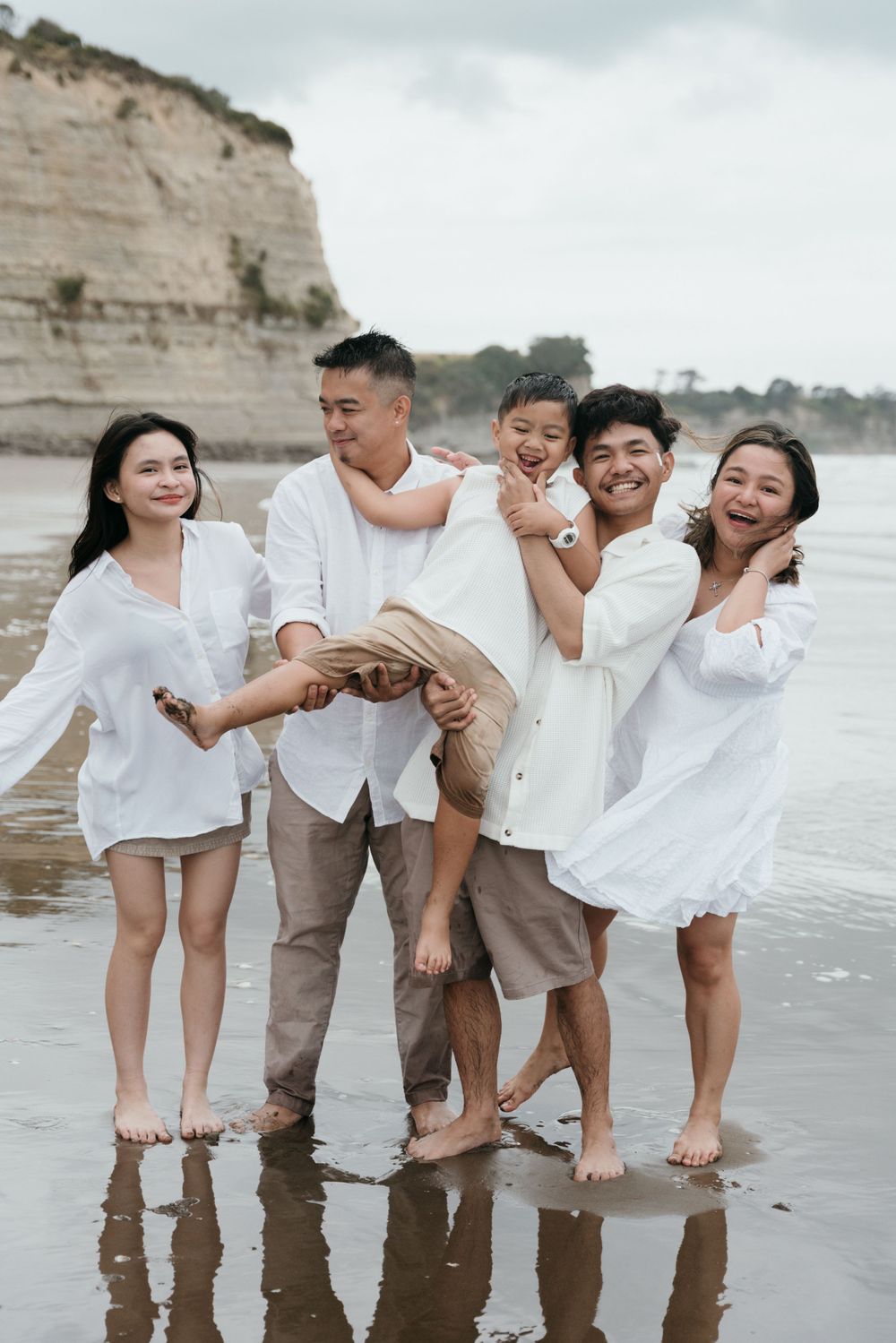 Happy group wearing white clothing plays together on beach near coastal cliffs.