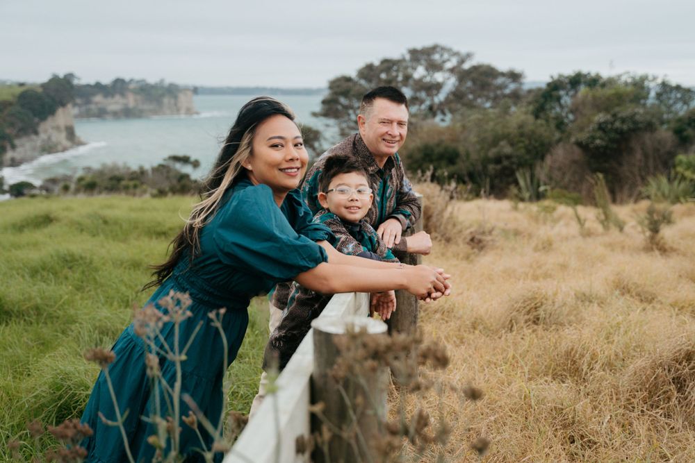 A joyful group leans against a railing overlooking coastal scenery on a sunny day.