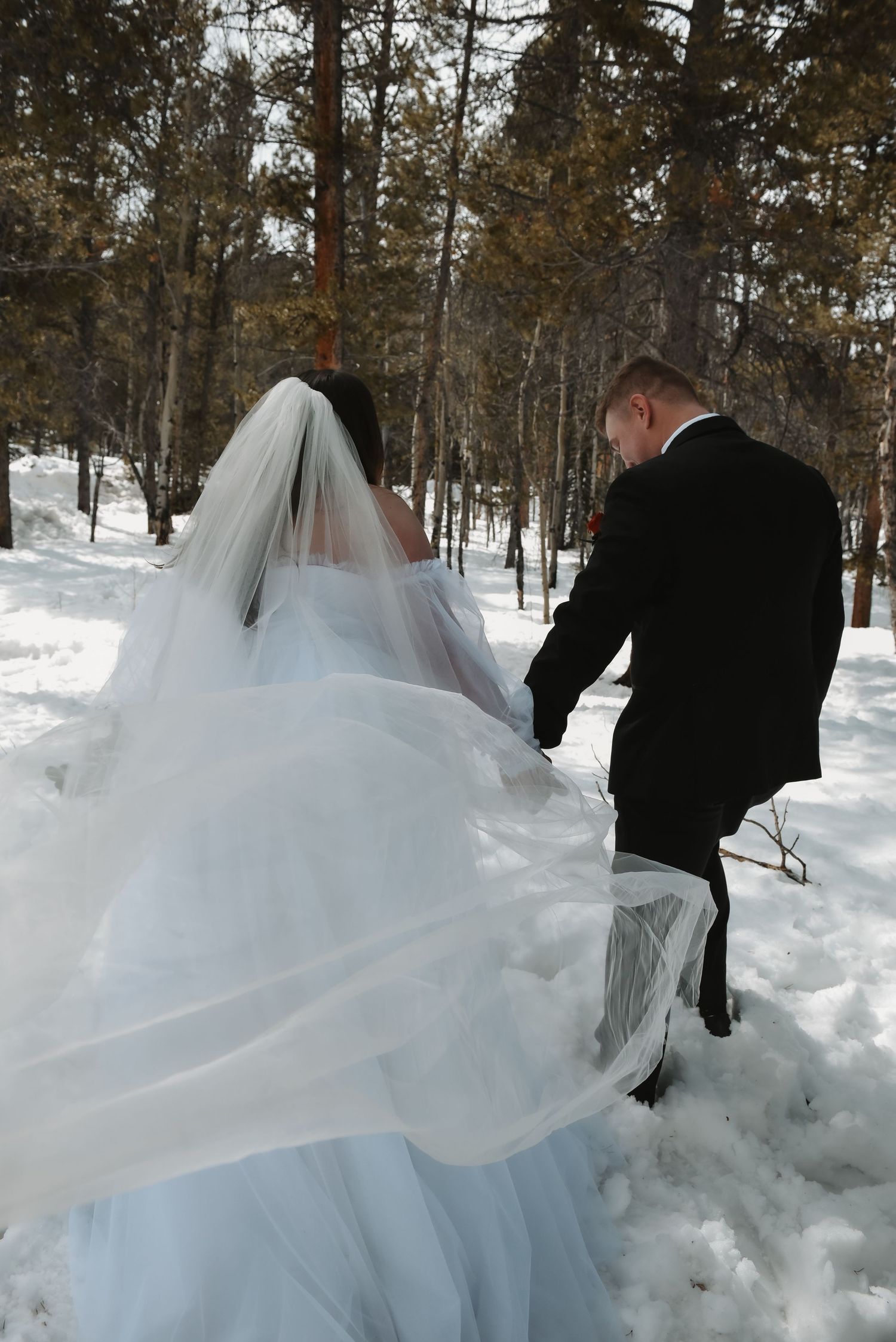 White wedding dress billows dramatically in the wind across snowy winter landscape during outdoor photo session.