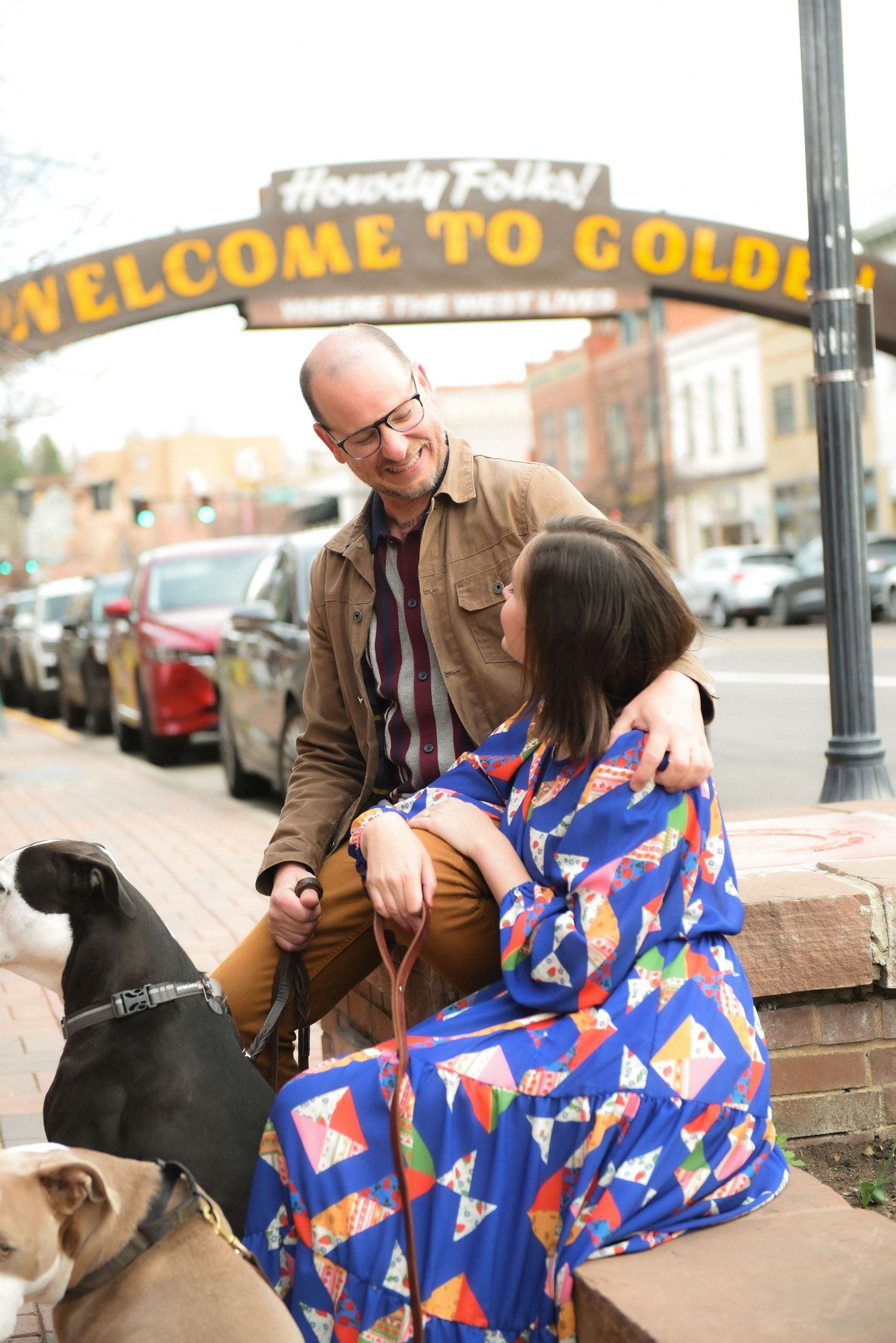 Someone sitting with a dog on city steps shares a bright blue patterned blanket with red and gold geometric designs.