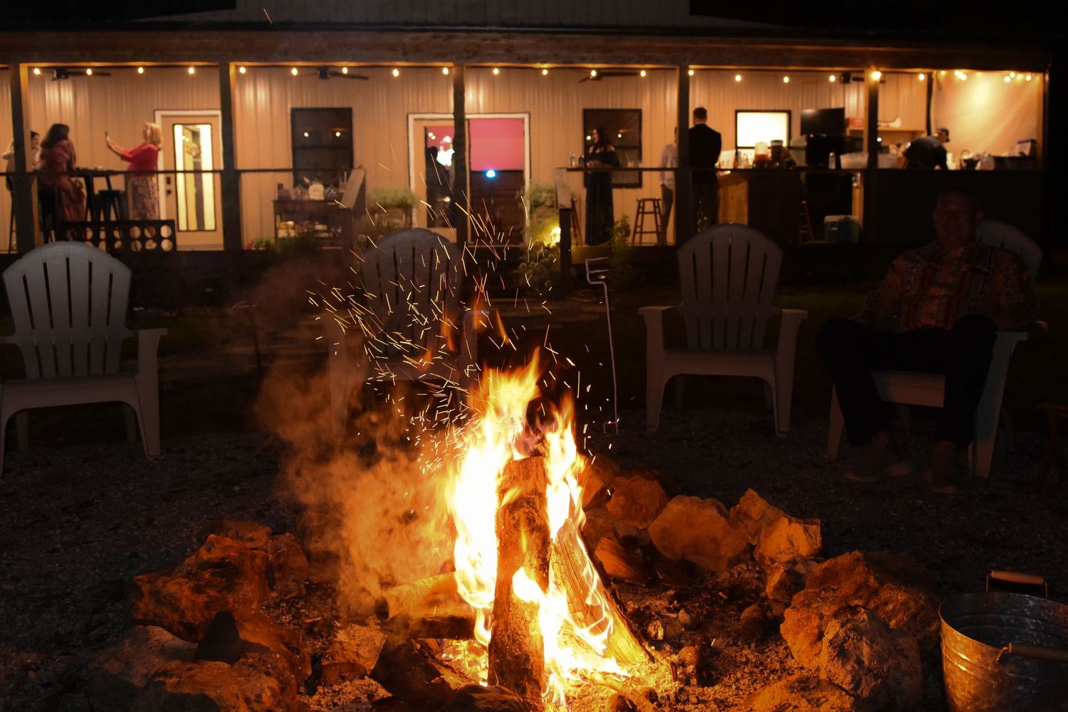Golden firelight illuminates a row of windows glowing warmly in the darkness as a bonfire burns in the foreground.
