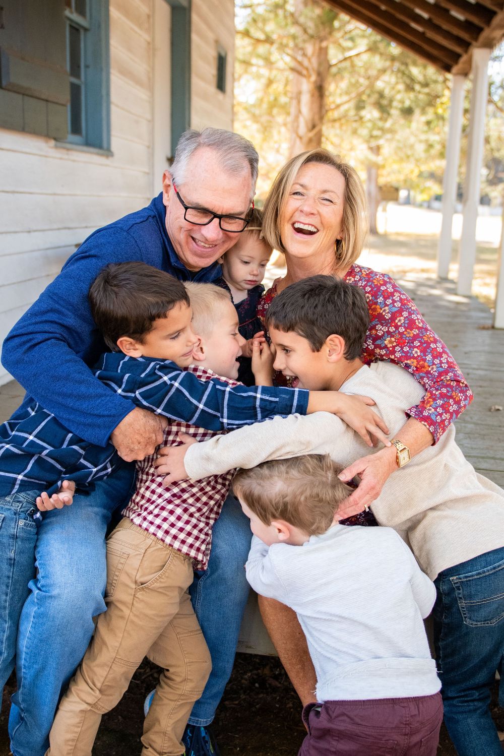 Playful candid family photoshoot showing joyful embraces and laughter against a rustic building backdrop.