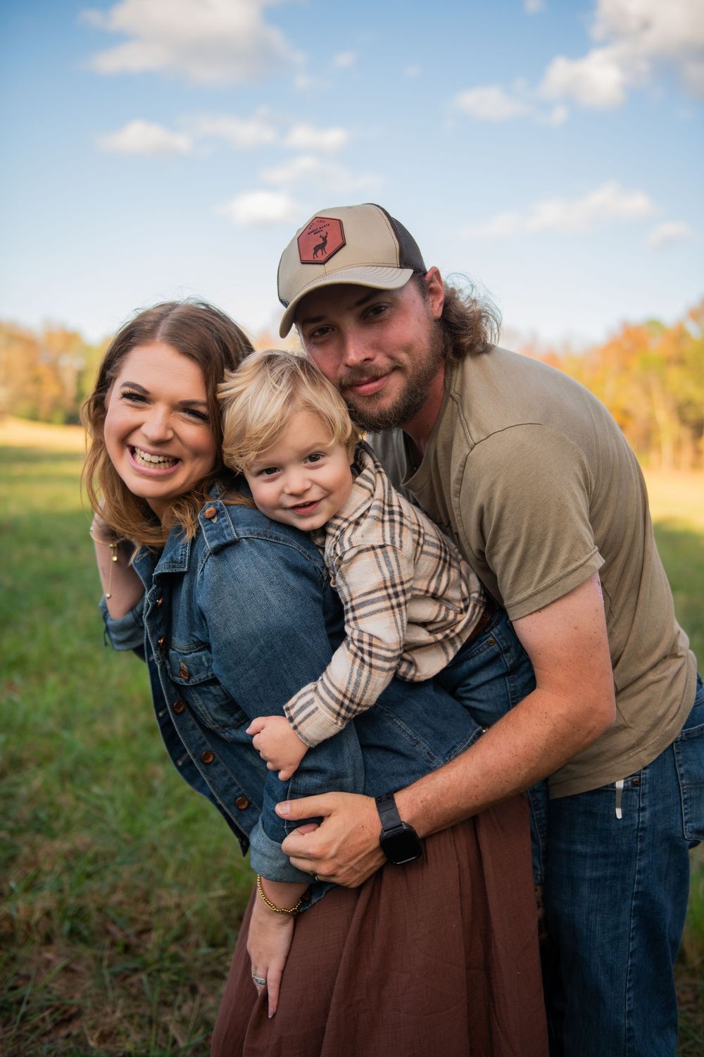 Family embracing and laughing together in field during golden hour.