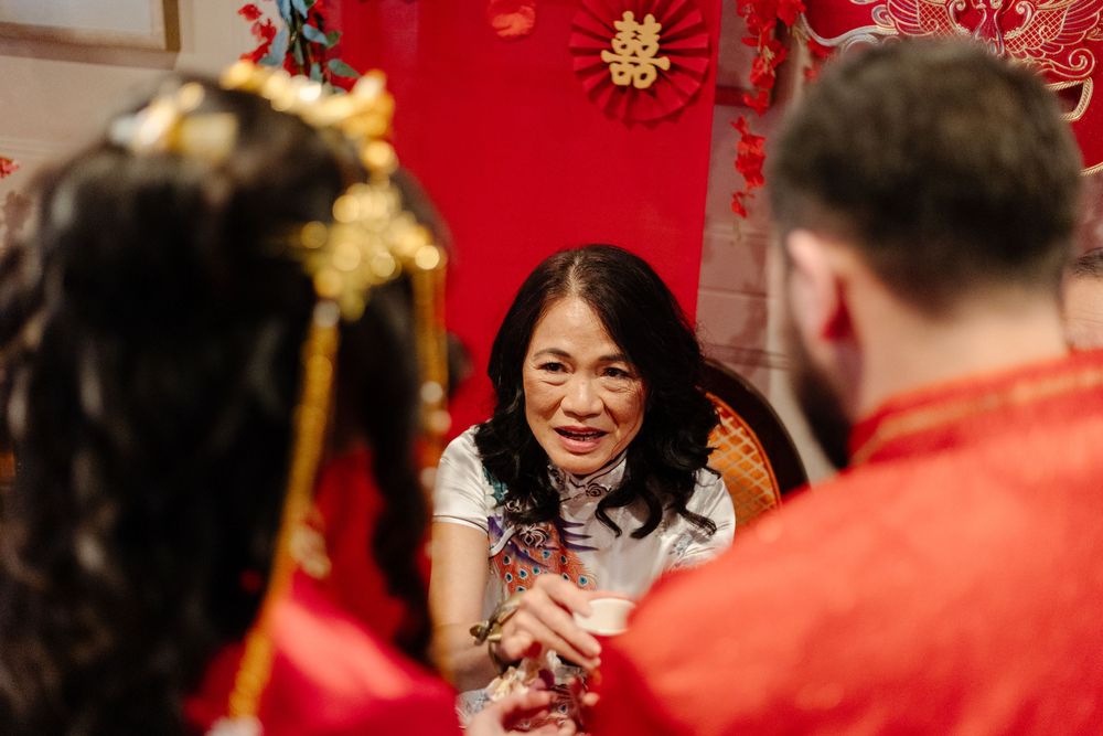 Elderly Asian woman smiling warmly during a traditional Chinese wedding tea ceremony, surrounded by red decor.