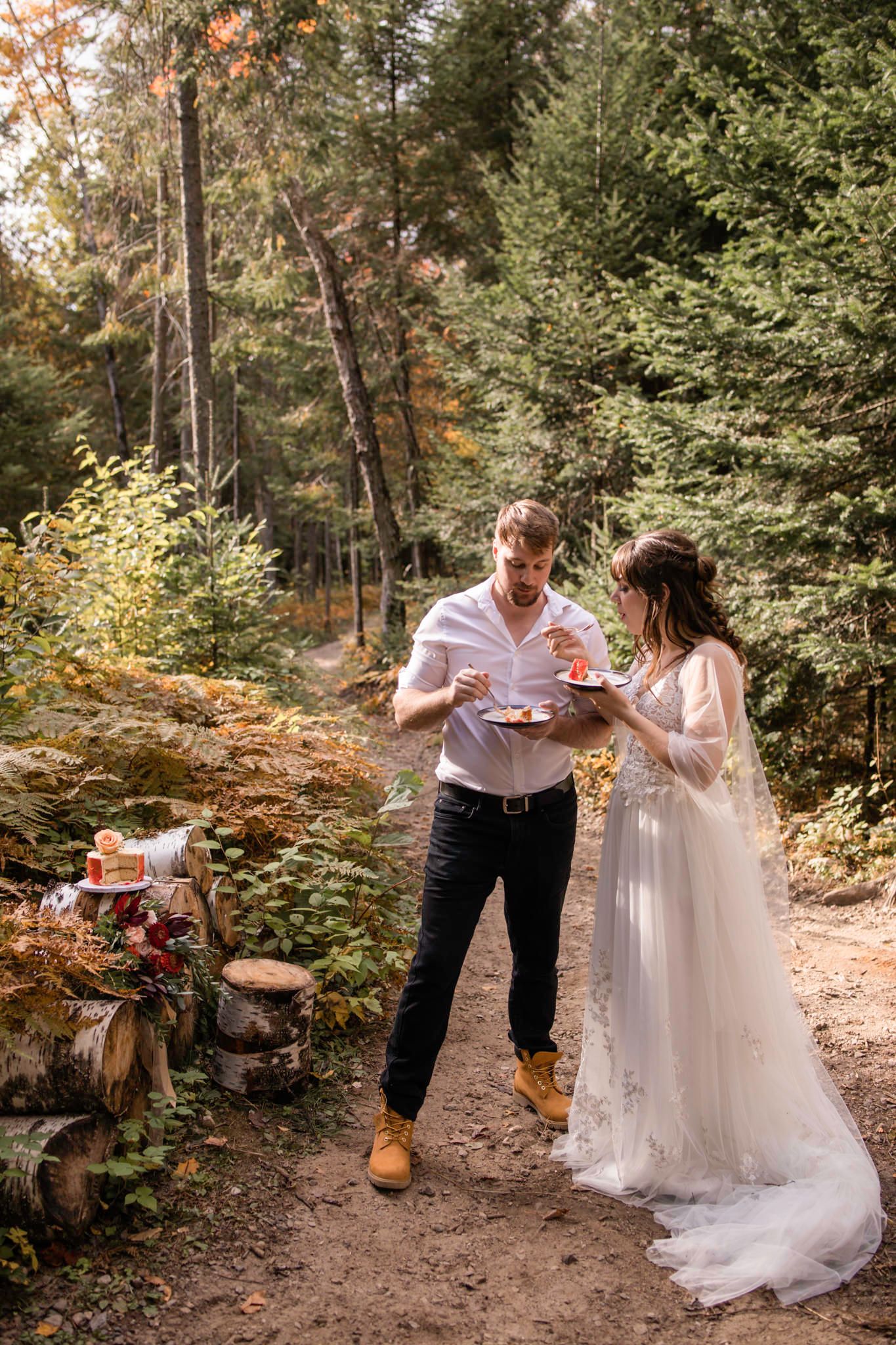 Eloping couple share cake to celebrate their marriage, standing in the forest in Mont Tremblant, Quebec, Canada.