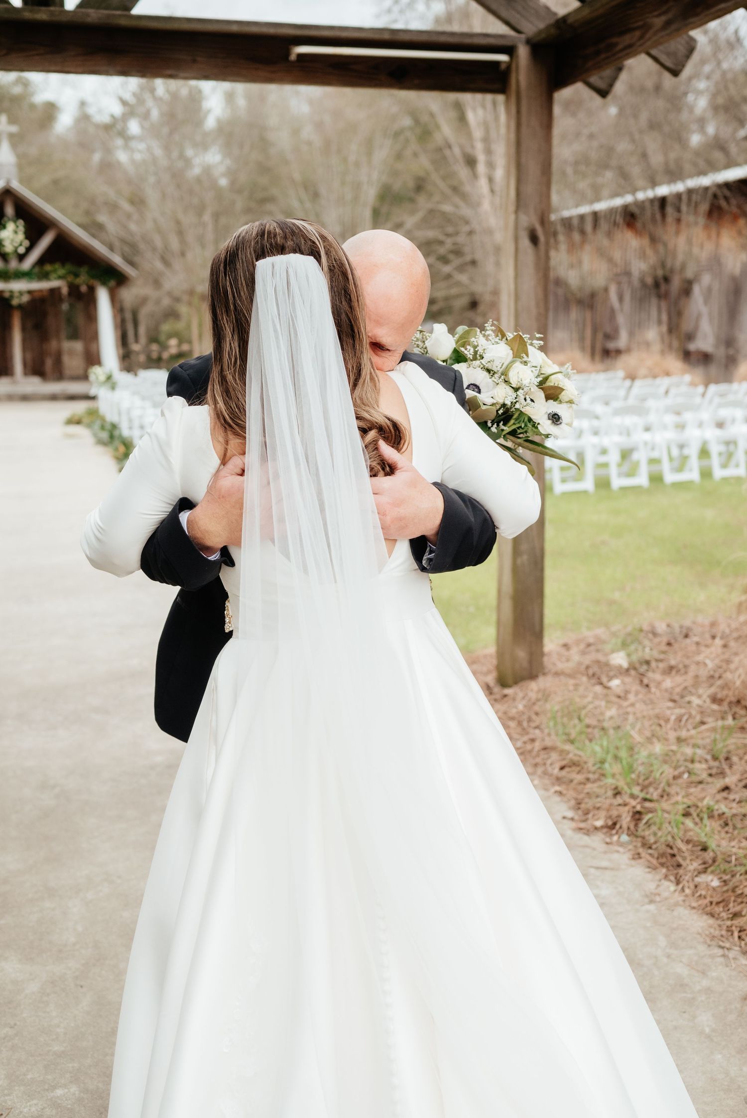 Bride and groom share emotional first look embrace outdoors at rustic wedding venue.
