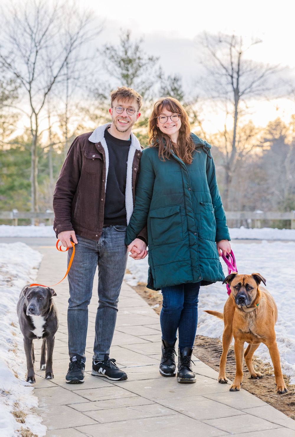 A couple and their two dogs pose together on a winter walking path.