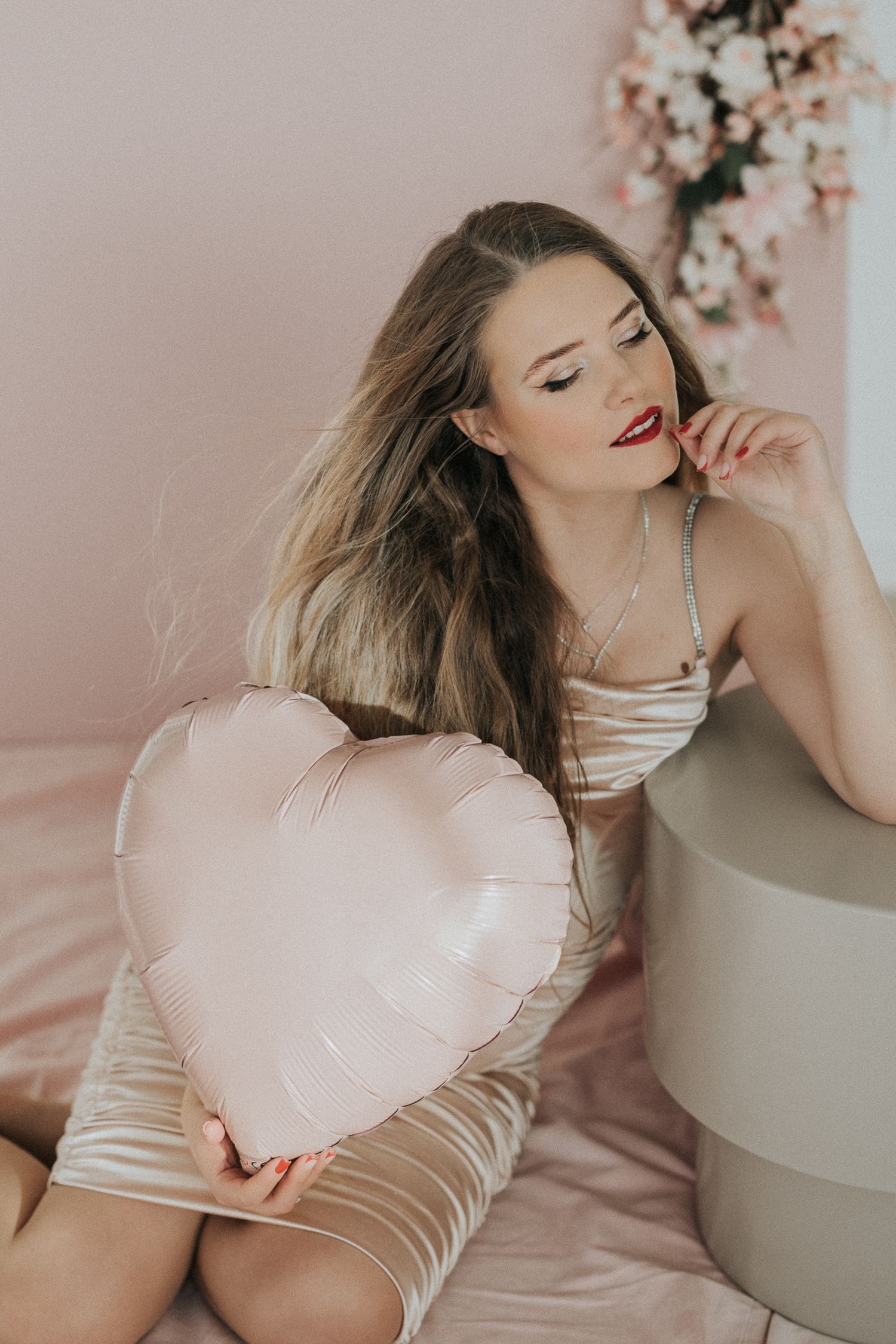 Young woman in satin dress holding pink heart balloon in romantic Valentine's Day photo shoot.