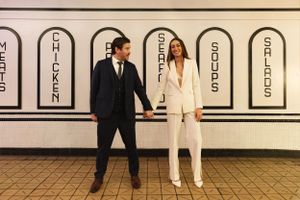 Stylish couple in contrasting black and white formal attire pose against a tiled wall with arched designs.