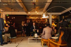 Crowded modern restaurant with warm lighting and industrial ceiling features showing people gathered in a social setting.