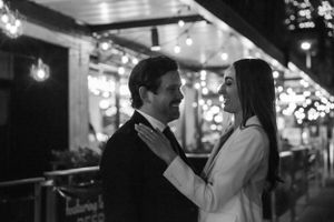 Black and white photo of couple embracing under outdoor string lights.