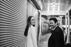 Black and white photo of couple standing by metal shutters in urban corridor.