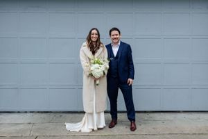 Wedding couple poses against grey garage door with white bouquet.