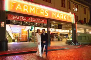 Evening scene at an illuminated Farmers Market entrance with 'Masks Required' signage.