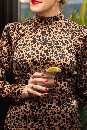 Woman in leopard print dress with red nails holds cocktail glass.