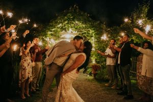 Wedding guests hold sparklers creating a magical nighttime tunnel for the newlyweds' kiss.