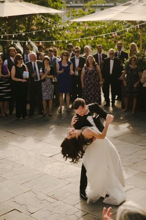 Couple performs romantic dip during first dance at outdoor wedding reception.